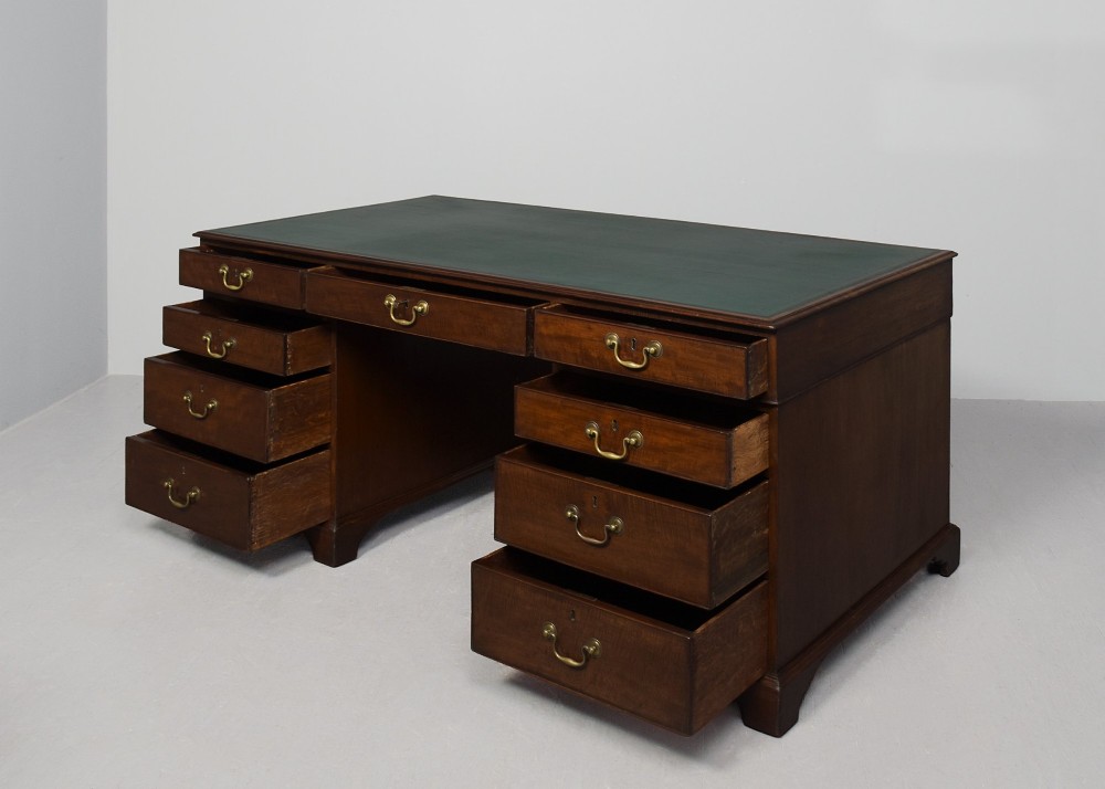 A large George III mahogany partners desk featuring a green leather writing surface, dual pedestals with brass swan-neck handles, and bracket feet. View V