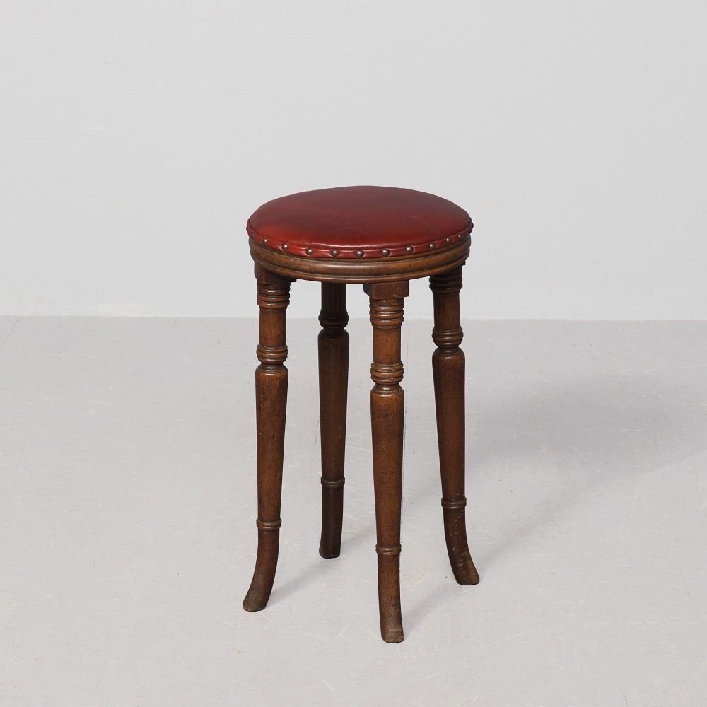 A tall George III circular wooden stool featuring four turned legs, a floral tapestry seat, and brass stud detailing along the rim.