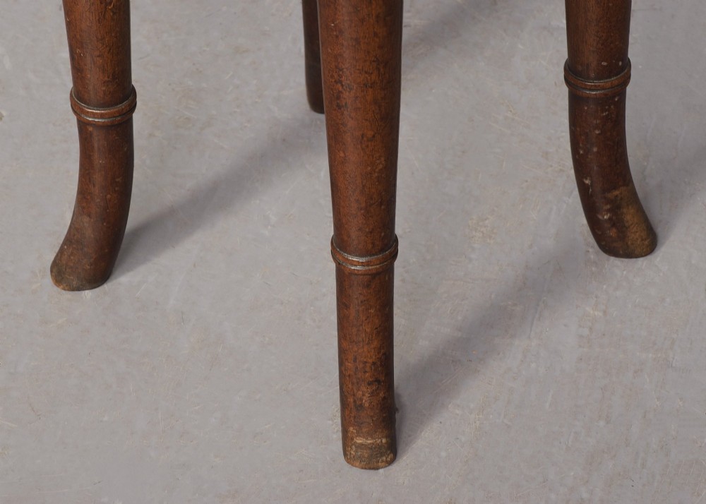 A tall George III circular wooden stool featuring four turned legs, a floral tapestry seat, and brass stud detailing along the rim. View V