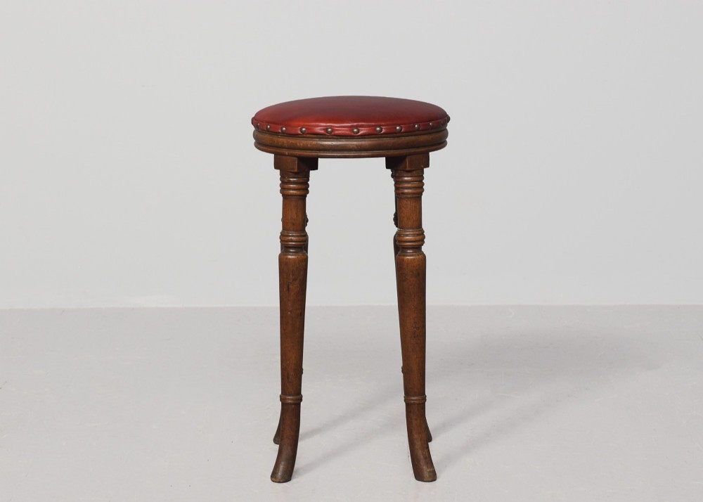 A tall George III circular wooden stool featuring four turned legs, a floral tapestry seat, and brass stud detailing along the rim. View VI