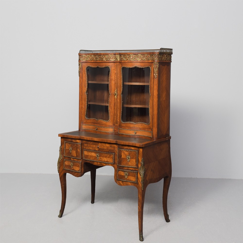 A nineteenth-century French style kingwood and walnut writing desk featuring an upper glazed display cabinet, brass top gallery, cabriole legs, and gilded metal mounts.