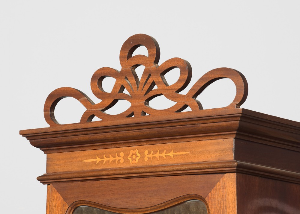 An Art Nouveau mahogany display cabinet featuring a central stained glass floral panel door, open side shelves with spindle supports, brass hardware, and round bullseye glass lower doors. View II