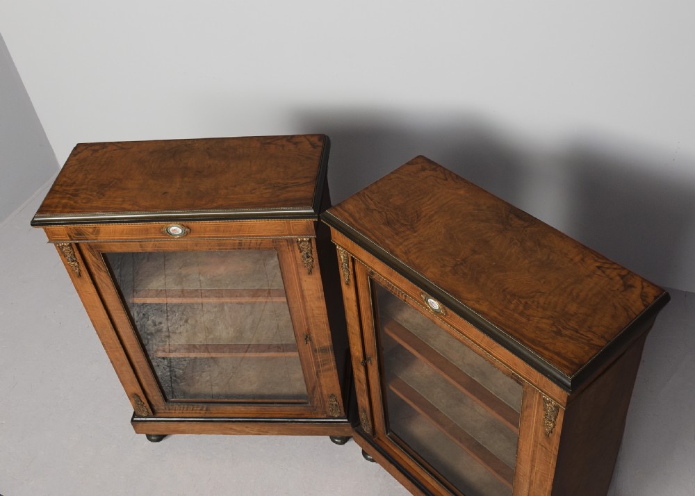 A pair of Victorian burr walnut pier cabinets with single glazed doors, ebonised trim, ormolu corner mounts, and oval porcelain plaques. View VI