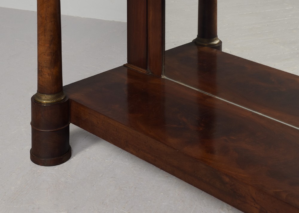 An early nineteenth-century French Empire mahogany console table featuring a light marble top, gilt brass column mounts, a mirrored back panel, and a lower shelf. View IV