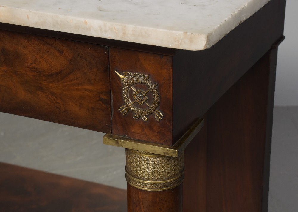 An early nineteenth-century French Empire mahogany console table featuring a light marble top, gilt brass column mounts, a mirrored back panel, and a lower shelf. View V
