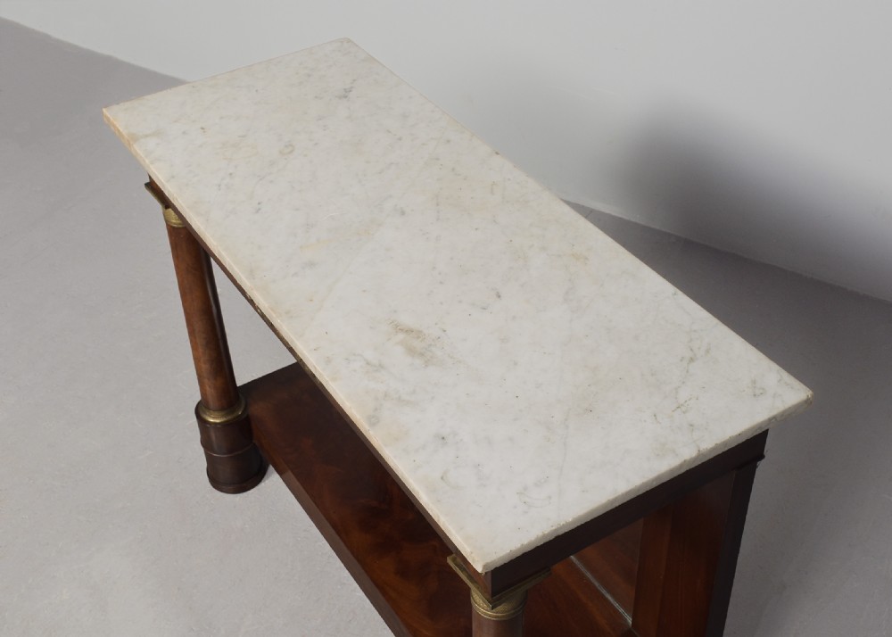 An early nineteenth-century French Empire mahogany console table featuring a light marble top, gilt brass column mounts, a mirrored back panel, and a lower shelf. View VI
