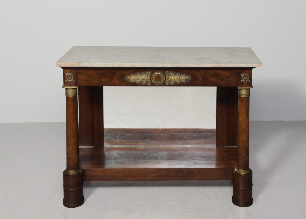 An early nineteenth-century French Empire mahogany console table featuring a light marble top, gilt brass column mounts, a mirrored back panel, and a lower shelf. View VII