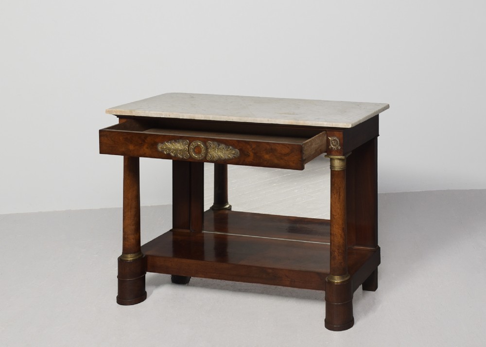 An early nineteenth-century French Empire mahogany console table featuring a light marble top, gilt brass column mounts, a mirrored back panel, and a lower shelf. View IX