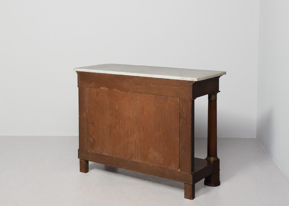 An early nineteenth-century French Empire mahogany console table featuring a light marble top, gilt brass column mounts, a mirrored back panel, and a lower shelf. View X
