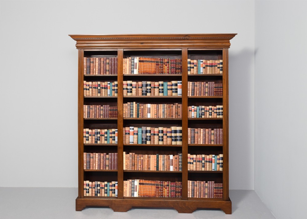 A tall mid-Victorian mahogany three-section open bookcase featuring a moulded top cornice and a solid plinth base filled with books.