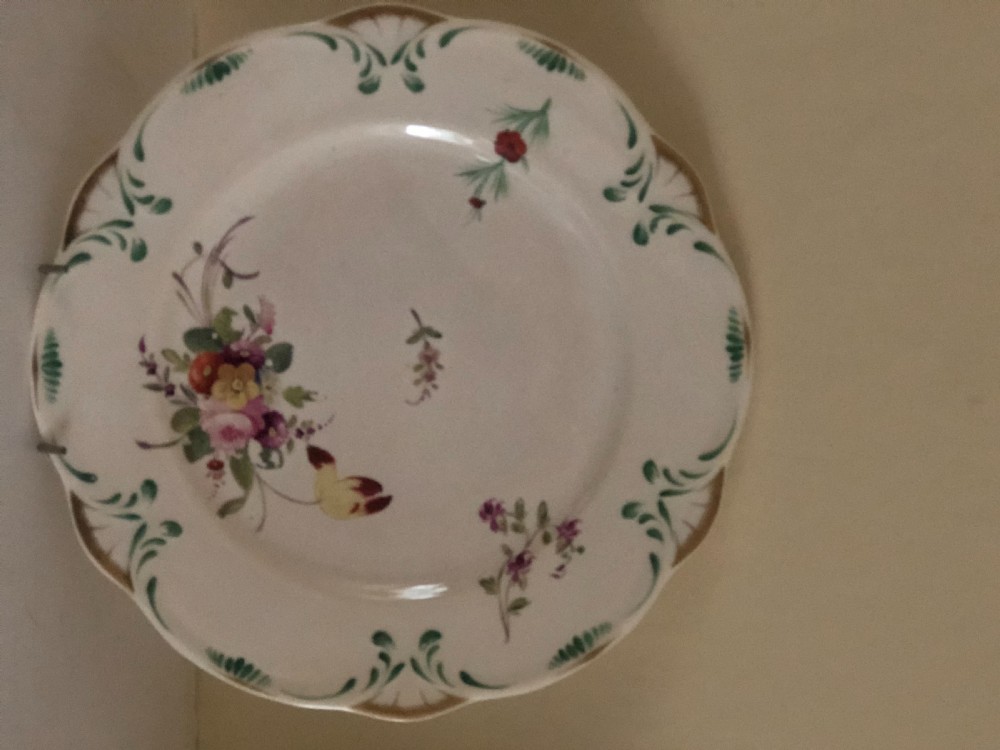 An antique circular white porcelain dessert plate featuring a scalloped edge with green scroll moulding, gilded details, and hand-painted floral sprays across the centre.