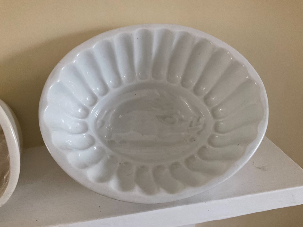 A row of four white glazed earthenware jelly moulds displaying distinct interior relief motifs including grapevines, flowers, and a boar. View II