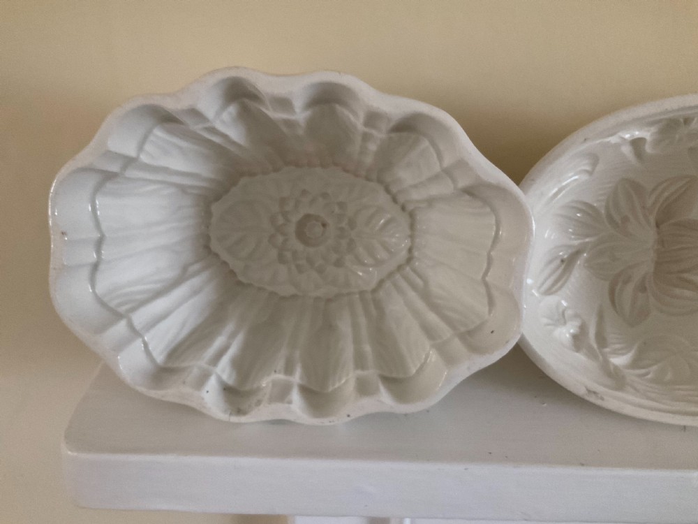 A row of four white glazed earthenware jelly moulds displaying distinct interior relief motifs including grapevines, flowers, and a boar. View VI