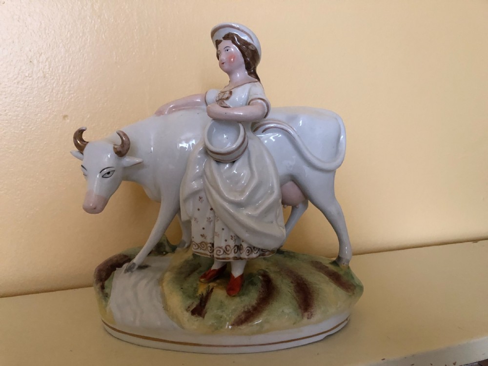 A pair of Victorian Staffordshire ceramic figures featuring a boy standing beside a white cow on one base, and a milkmaid with a pail beside a cow on the other base. View III