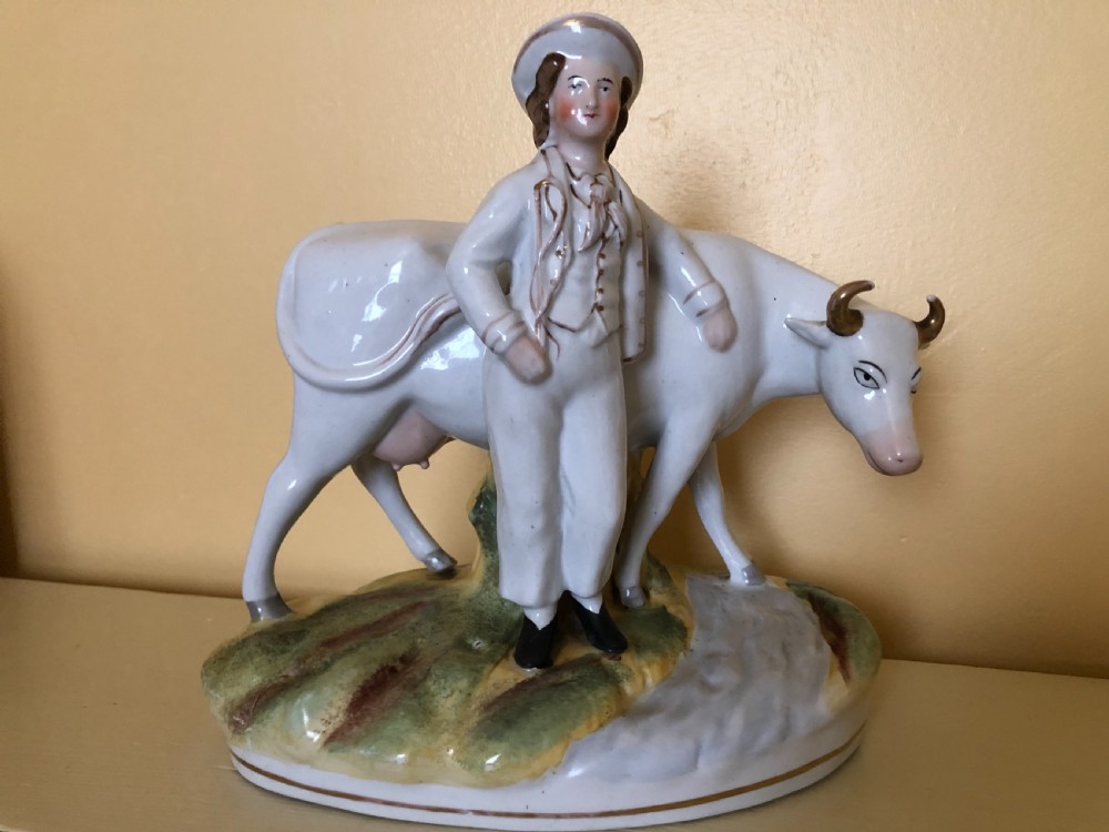 A pair of Victorian Staffordshire ceramic figures featuring a boy standing beside a white cow on one base, and a milkmaid with a pail beside a cow on the other base. View IV