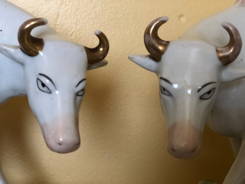 A pair of Victorian Staffordshire ceramic figures featuring a boy standing beside a white cow on one base, and a milkmaid with a pail beside a cow on the other base. View V