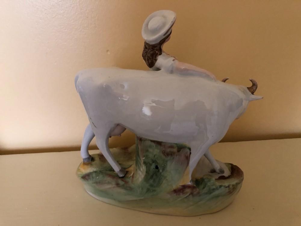 A pair of Victorian Staffordshire ceramic figures featuring a boy standing beside a white cow on one base, and a milkmaid with a pail beside a cow on the other base. View VI