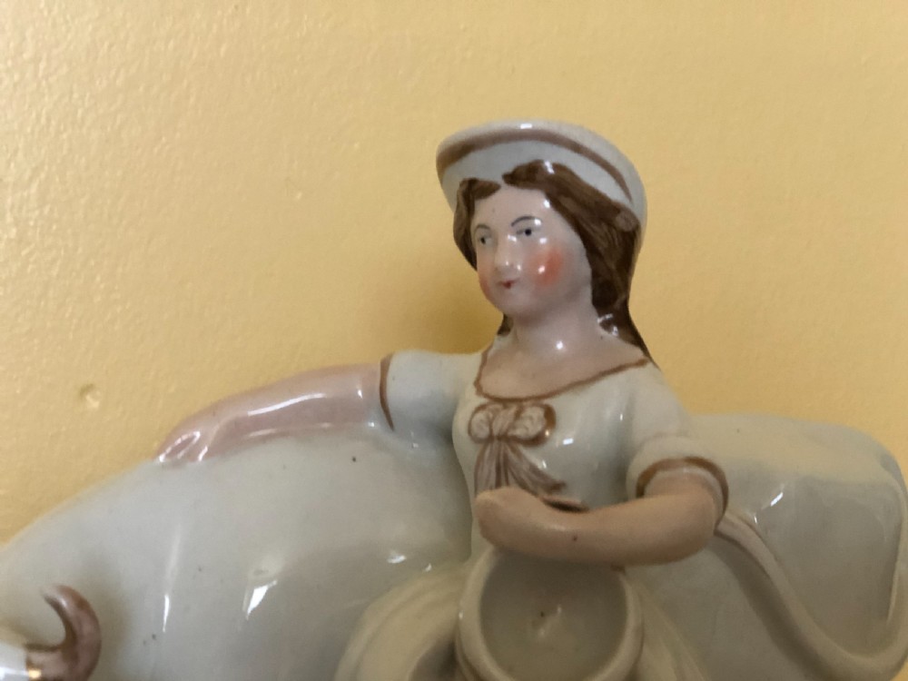 A pair of Victorian Staffordshire ceramic figures featuring a boy standing beside a white cow on one base, and a milkmaid with a pail beside a cow on the other base. View VII