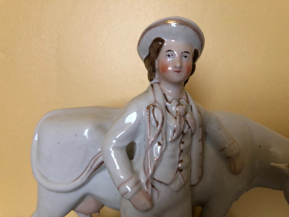 A pair of Victorian Staffordshire ceramic figures featuring a boy standing beside a white cow on one base, and a milkmaid with a pail beside a cow on the other base. View VIII