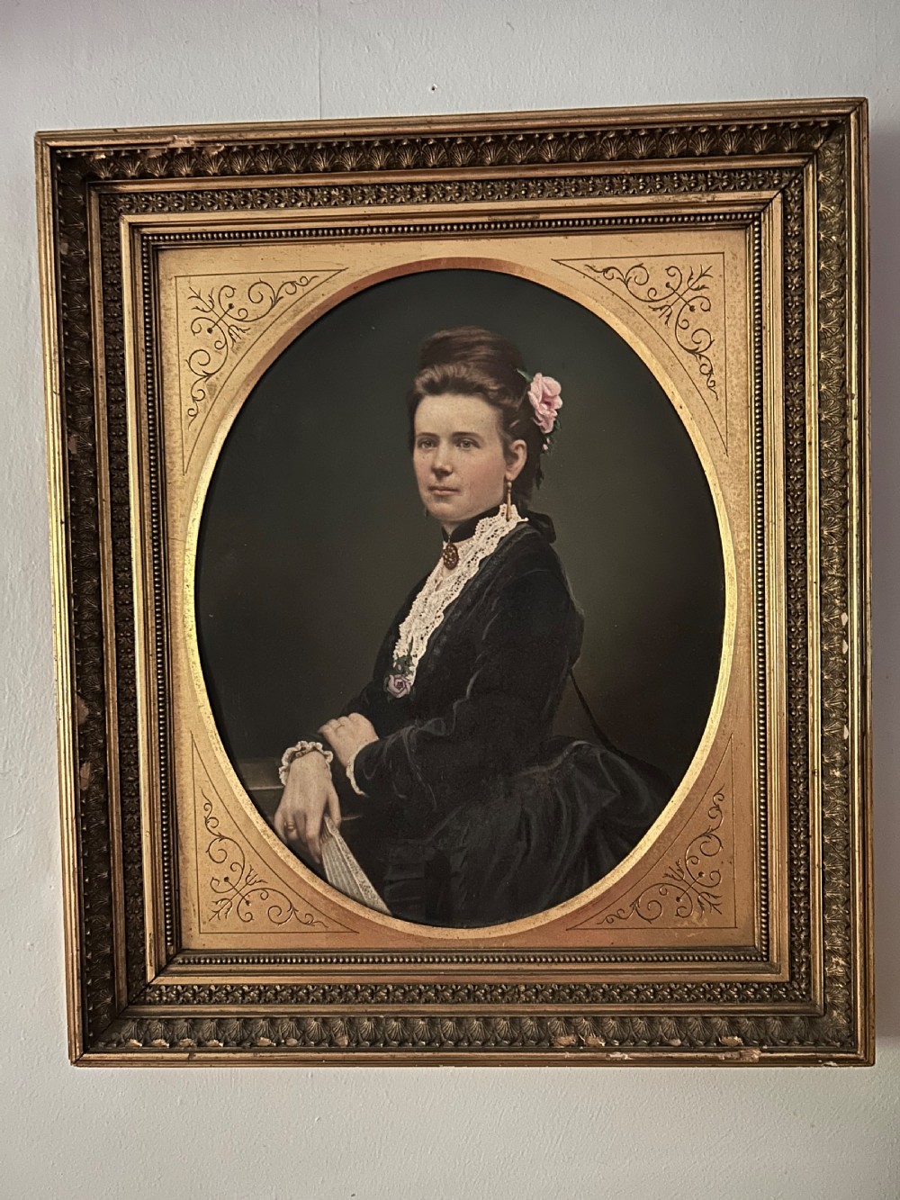 A nineteenth-century oil portrait of a woman in a black dress with lace detail, presented inside an oval gold mount and an ornate carved giltwood frame.
