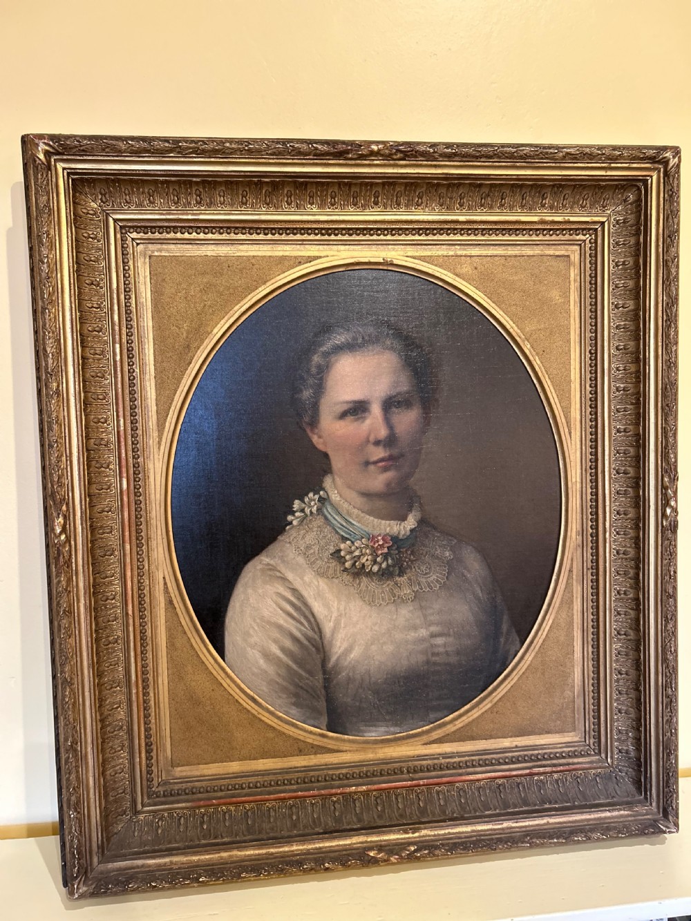 A late nineteenth-century oil portrait depicting a woman in a light dress within an oval mount and ornate rectangular gilt frame.