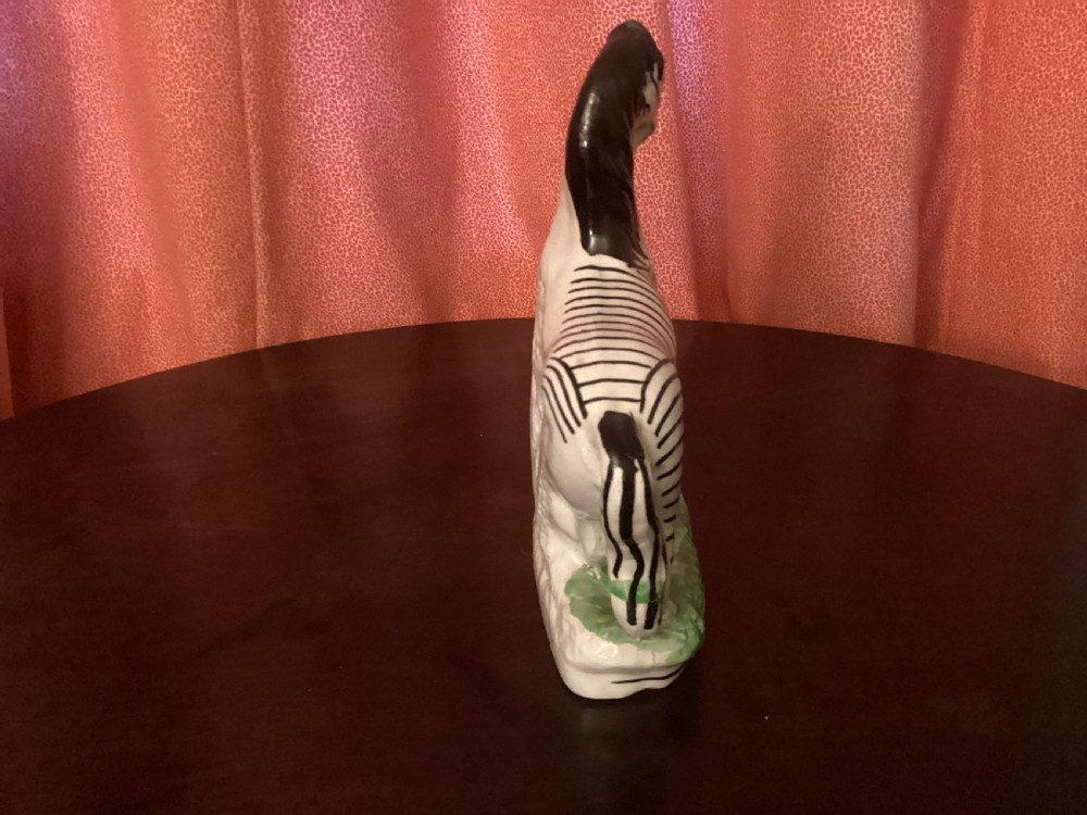 A 19th-century Staffordshire earthenware ceramic figure of a zebra with hand-painted black stripes standing on a green grass-like base. View III