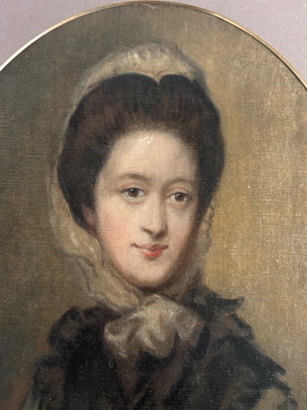 A late eighteenth-century oval oil portrait depicting a woman wearing a bonnet and dark mantle, presented inside a gilded frame. View II