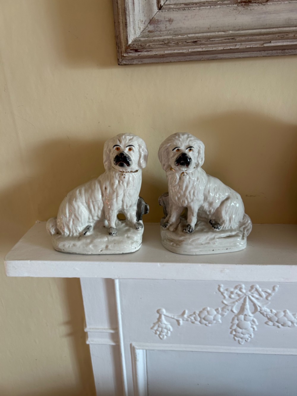 A pair of white glazed earthenware Staffordshire dog figurines modelled as seated Maltese terriers with hand-painted black and orange facial features.