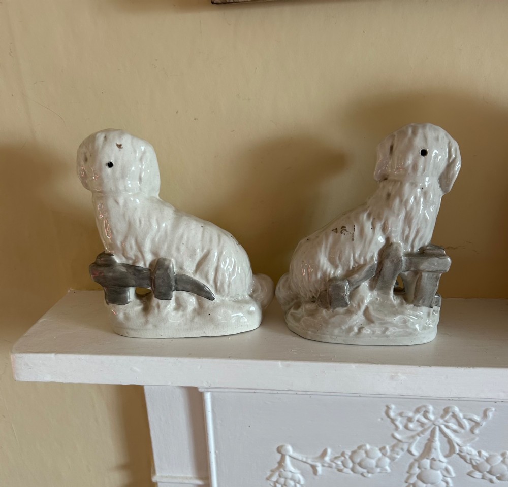 A pair of white glazed earthenware Staffordshire dog figurines modelled as seated Maltese terriers with hand-painted black and orange facial features. View II