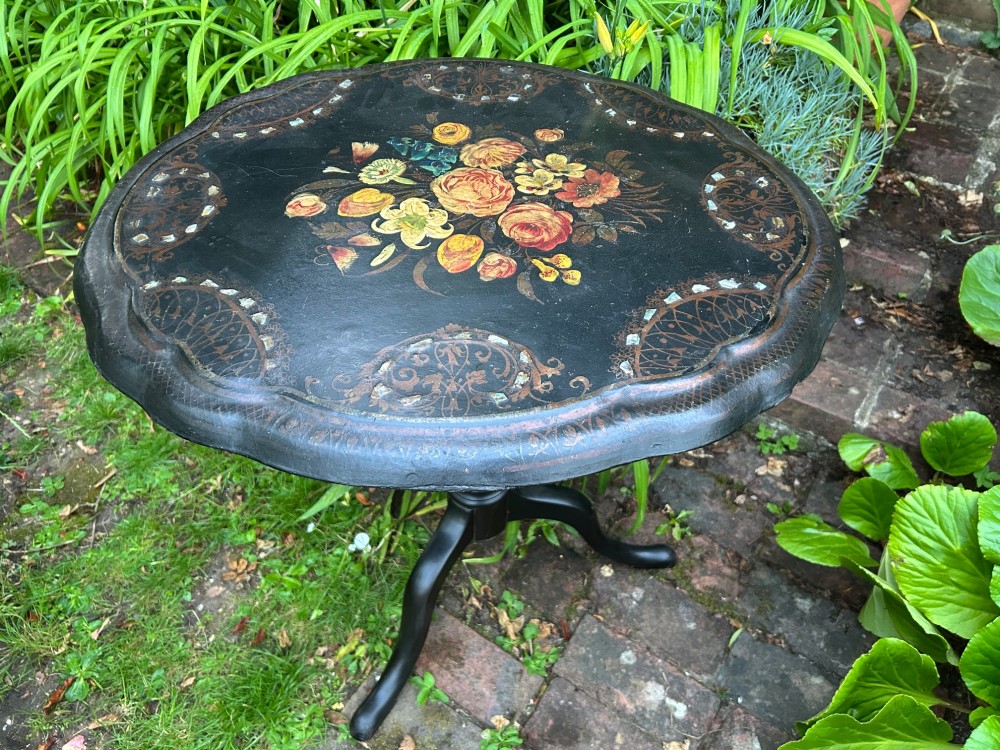 A Victorian black papier mache wine table featuring hand-painted botanical motifs, mother-of-pearl inlay, a scalloped edge, and a tripod base.