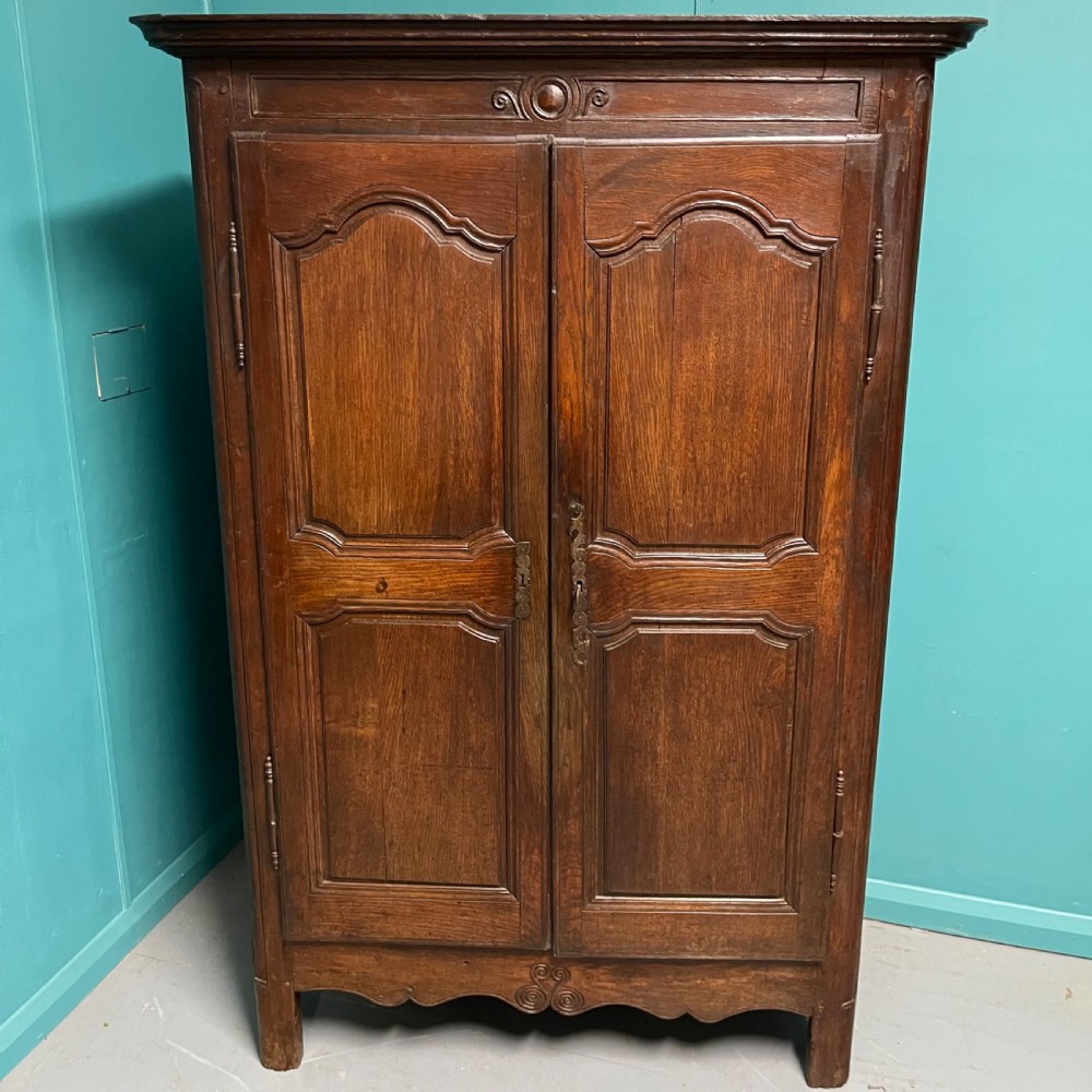 An 18th-century low French oak armoire featuring two fielded panel doors, carved frieze details, and long iron exterior hinges.