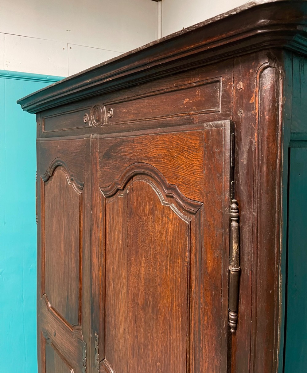 An 18th-century low French oak armoire featuring two fielded panel doors, carved frieze details, and long iron exterior hinges. View IV