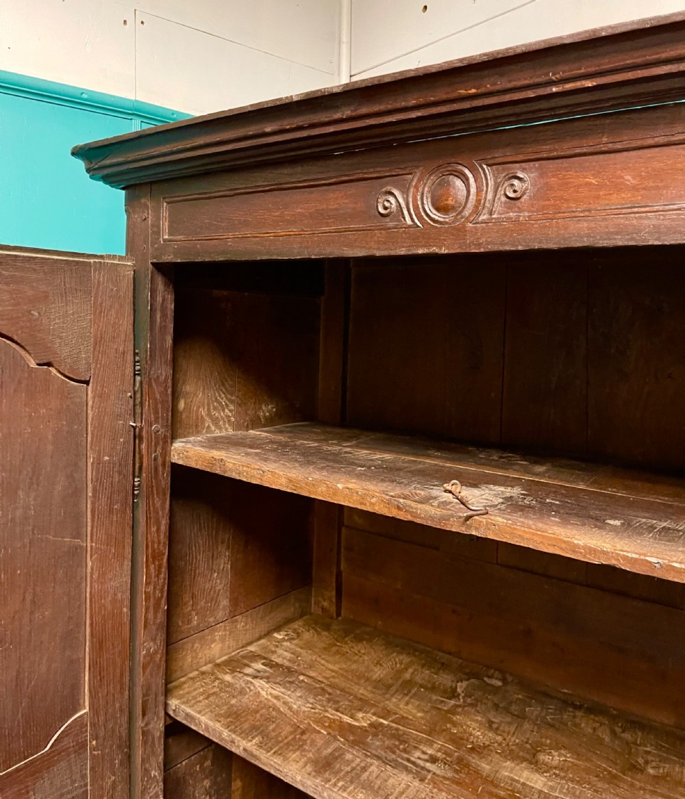 An 18th-century low French oak armoire featuring two fielded panel doors, carved frieze details, and long iron exterior hinges. View VI