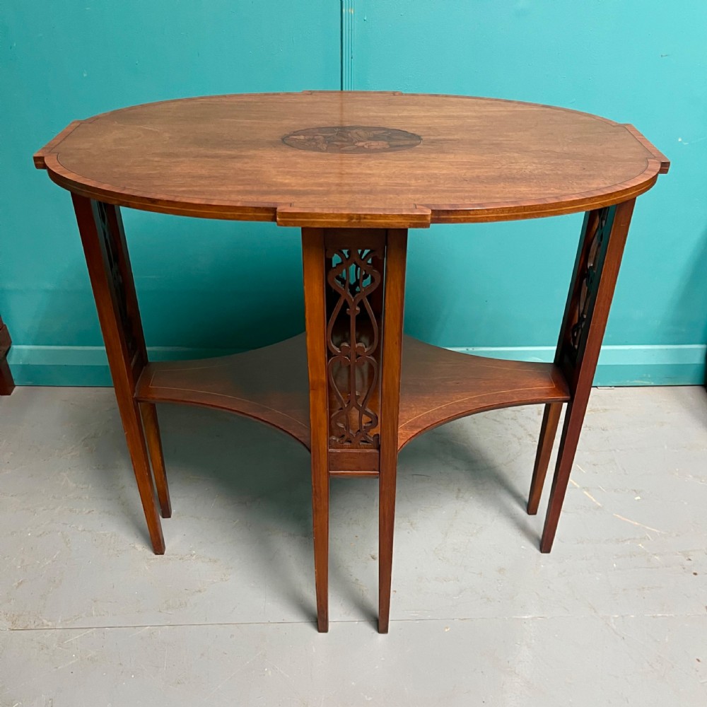 An Edwardian oval wooden side table featuring a central floral marquetry medallion, crossbanded border, pierced fretwork side aprons, and an under-shelf. View II