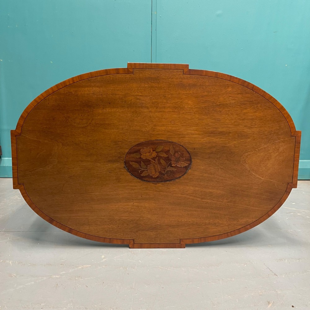 An Edwardian oval wooden side table featuring a central floral marquetry medallion, crossbanded border, pierced fretwork side aprons, and an under-shelf. View III
