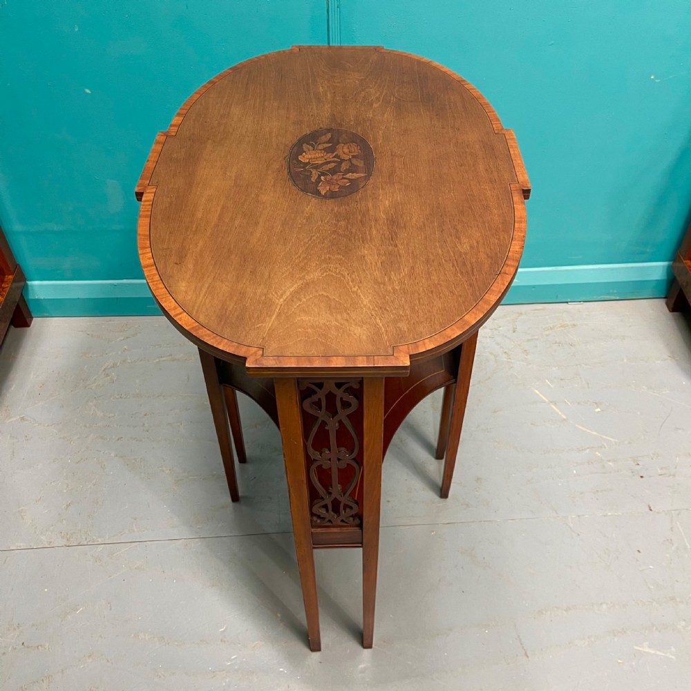 An Edwardian oval wooden side table featuring a central floral marquetry medallion, crossbanded border, pierced fretwork side aprons, and an under-shelf. View VI