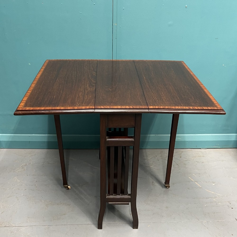 An Edwardian dark mahogany drop-leaf Sutherland table featuring satinwood crossbanding around the tabletop edge and slender gate-leg supports. View V