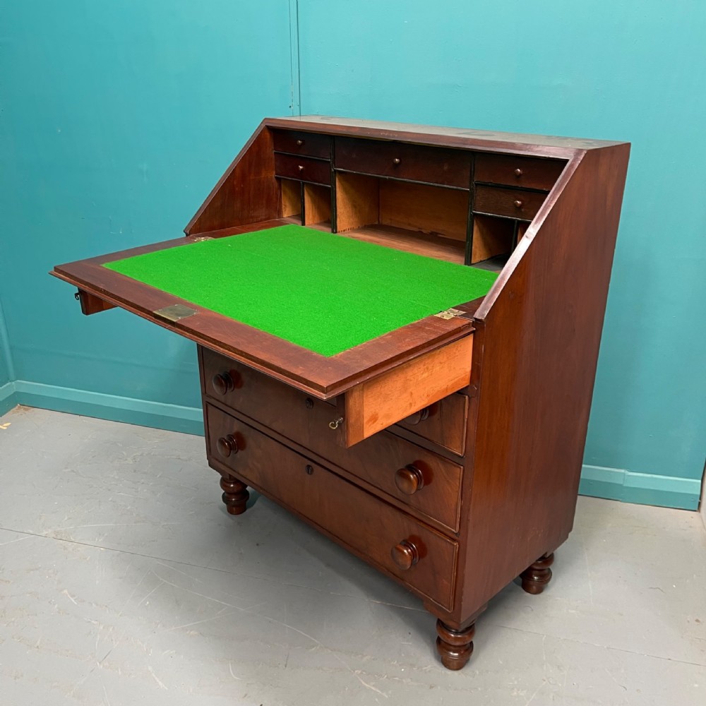 An early Victorian mahogany writing bureau with an open sloping flap revealing a green writing surface and internal pigeonholes, resting on turned feet.