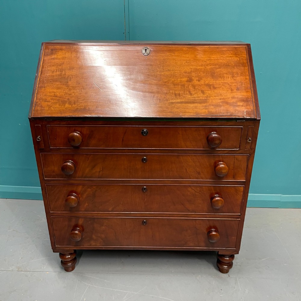 An early Victorian mahogany writing bureau with an open sloping flap revealing a green writing surface and internal pigeonholes, resting on turned feet. View V