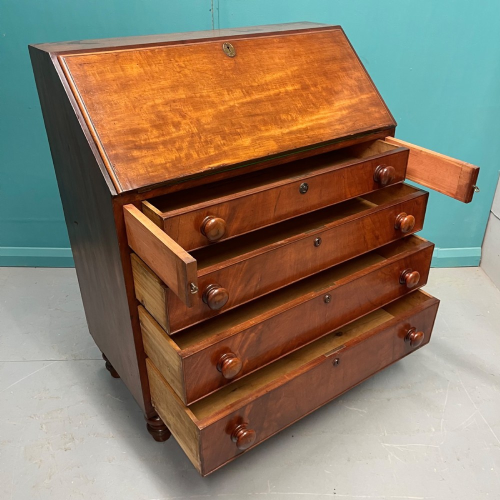 An early Victorian mahogany writing bureau with an open sloping flap revealing a green writing surface and internal pigeonholes, resting on turned feet. View VIII