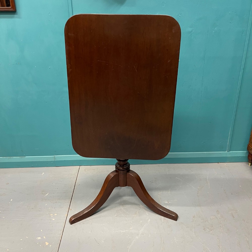 An antique dark mahogany tilt-top side table displayed in its vertical position on a turned column with three downswept legs.