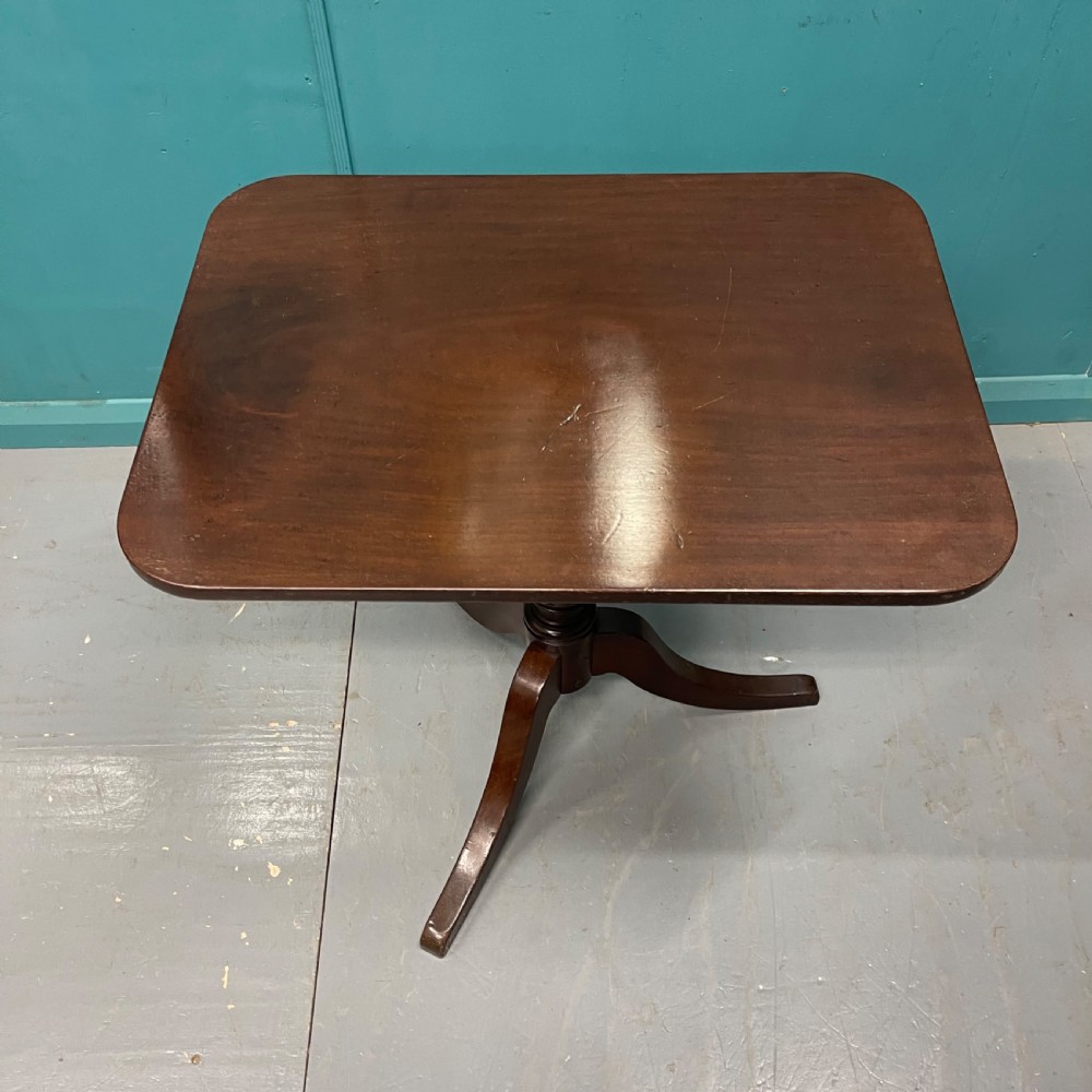 An antique dark mahogany tilt-top side table displayed in its vertical position on a turned column with three downswept legs. View II