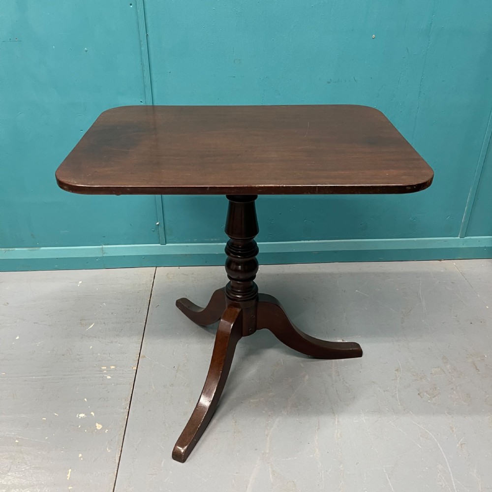 An antique dark mahogany tilt-top side table displayed in its vertical position on a turned column with three downswept legs. View III