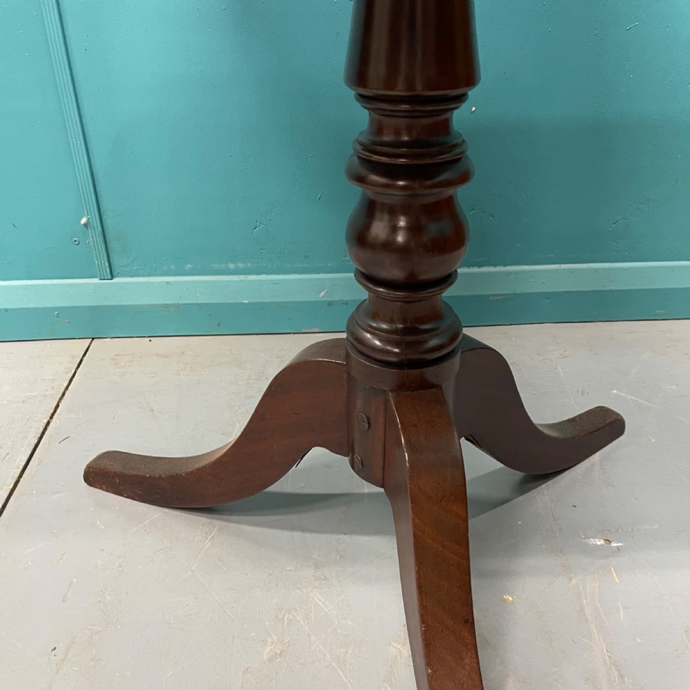An antique dark mahogany tilt-top side table displayed in its vertical position on a turned column with three downswept legs. View IV