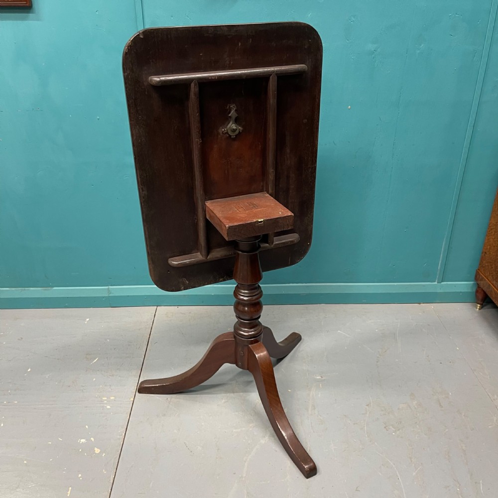 An antique dark mahogany tilt-top side table displayed in its vertical position on a turned column with three downswept legs. View V