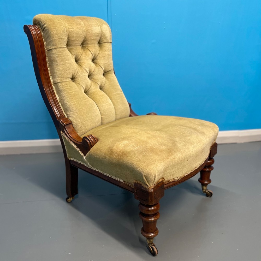 A William IV slipper chair upholstered in olive green velvet with deep button tufting, a scroll back, and turned mahogany front legs on brass castors.