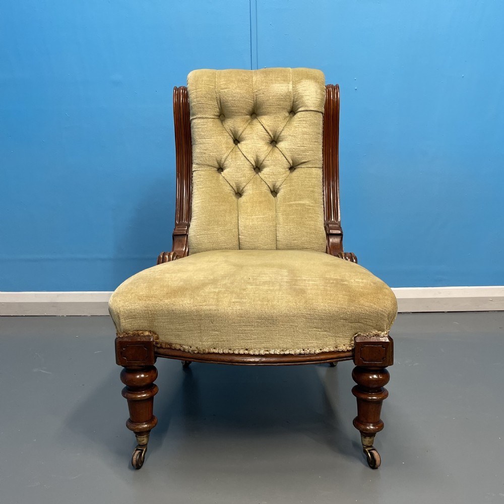 A William IV slipper chair upholstered in olive green velvet with deep button tufting, a scroll back, and turned mahogany front legs on brass castors. View II