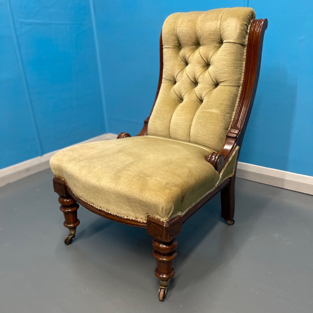A William IV slipper chair upholstered in olive green velvet with deep button tufting, a scroll back, and turned mahogany front legs on brass castors. View III