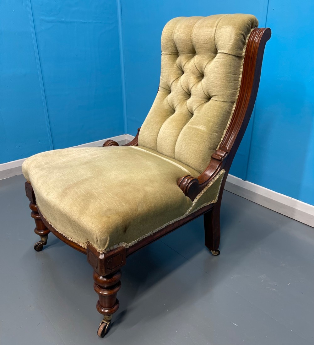 A William IV slipper chair upholstered in olive green velvet with deep button tufting, a scroll back, and turned mahogany front legs on brass castors. View V