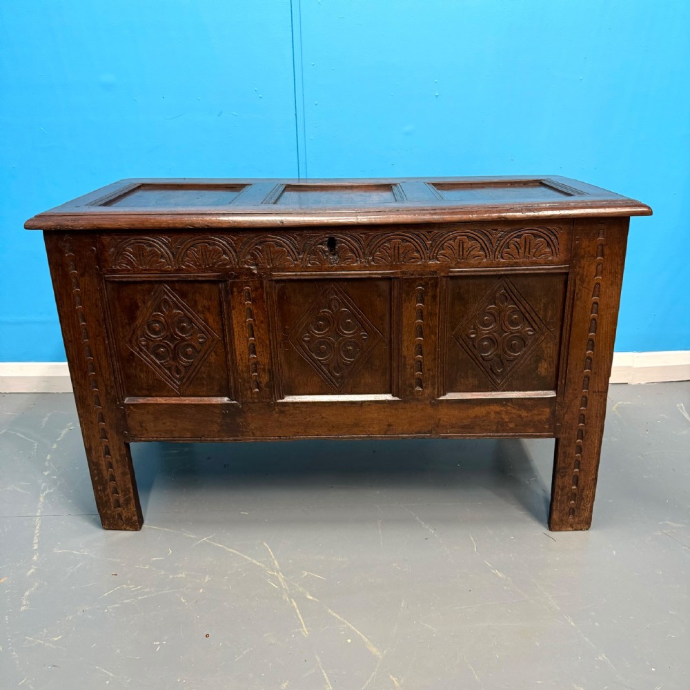 An 18th-century dark oak coffer featuring three carved diamond lozenge panels, an arcaded top rail, and a panelled hinged lid.